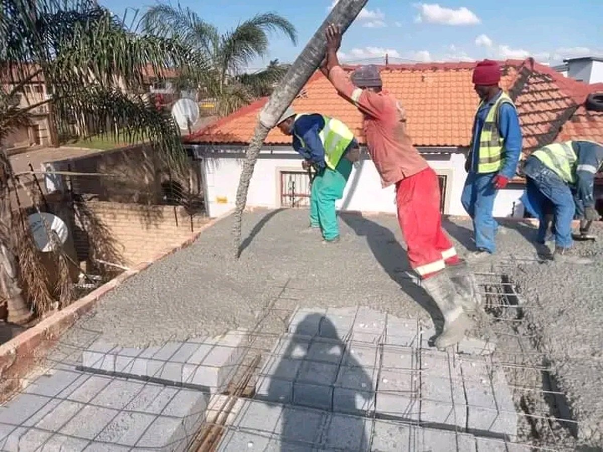 Construction workers pouring concrete onto roof slab with pump hose