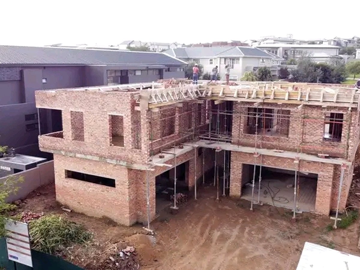 Two-story brick house construction with scaffolding and workers on site