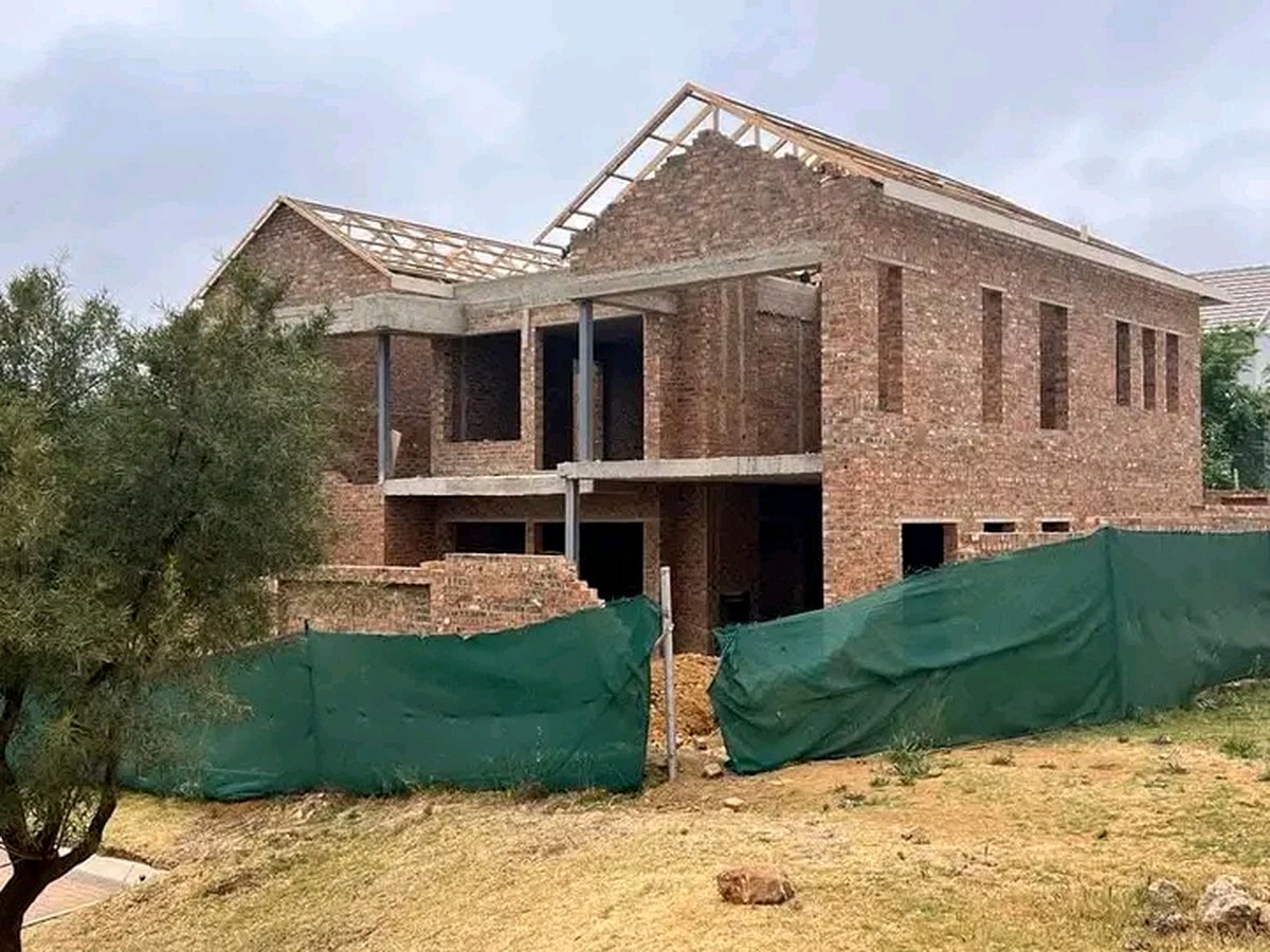 Two-story brick house with roof trusses installed and green construction fence